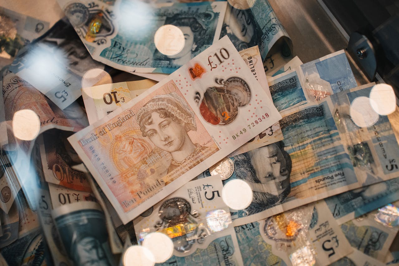 A detailed view of British £5 and £10 pound sterling notes with coins, featuring warm bokeh effects.