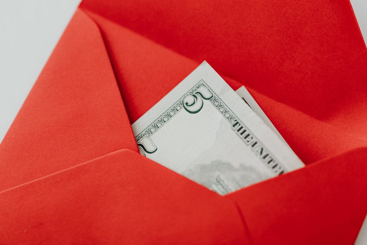 A close-up of a US dollar bill partially visible in a bright red envelope, symbolizing gifting or financial reward.